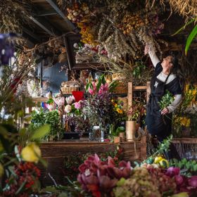 A staff member of Flowers Manuela reached into a bouquet in a room full of vibrant flowers.