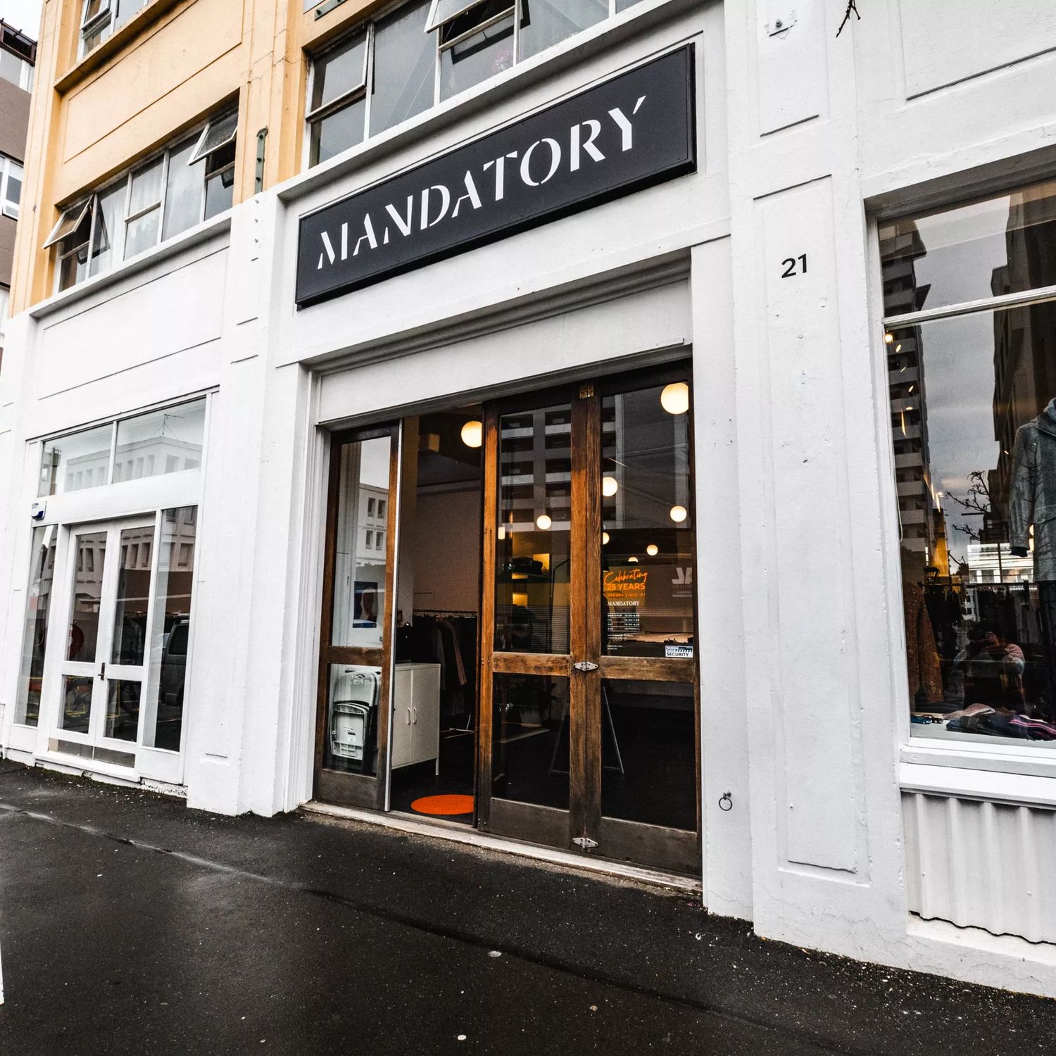 The exterior of Mandatory, with wooden doors and white painting outside. Mannequins are seen in the windows wearing their clothing.