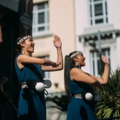 Three members of Hiwa, a Māori cultural group, perform on an outdoor stage at CubaDupa.