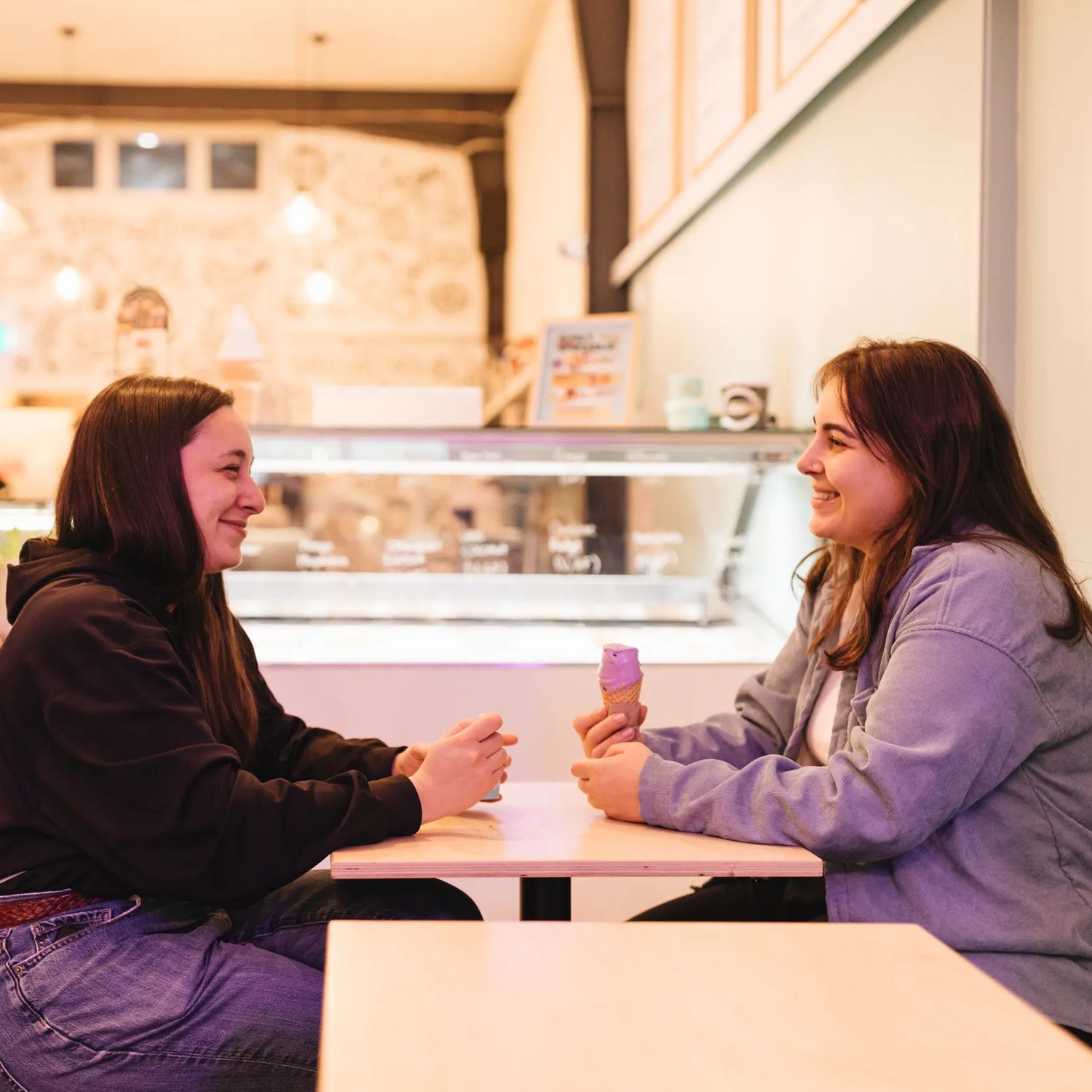 Two people hold ice creams and sit across from each other chatting inside Zelati on Cuba Street.