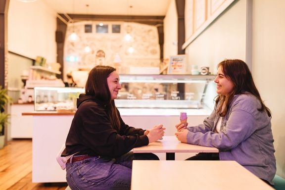 Two people hold ice creams and sit across from each other chatting inside Zelati on Cuba Street.