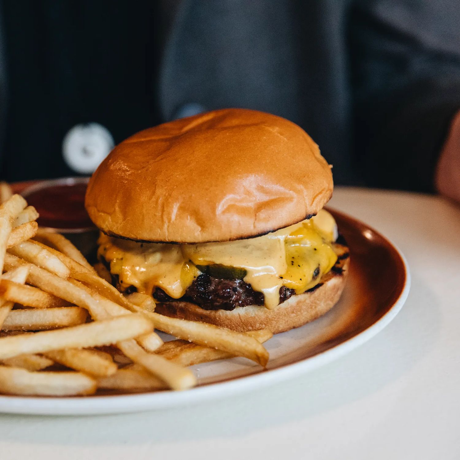 A close up of a juicy burger with melting cheese on a plate, with shoestring fries