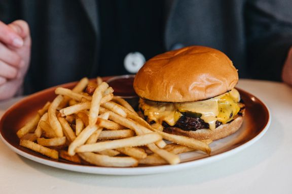 A close up of a juicy burger with melting cheese on a plate, with shoestring fries