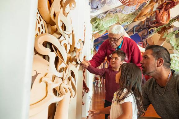 Two children and two adults are in a Maori exhibition in Te Papa Museum in Wellington admiring the woodwork that's displayed. 