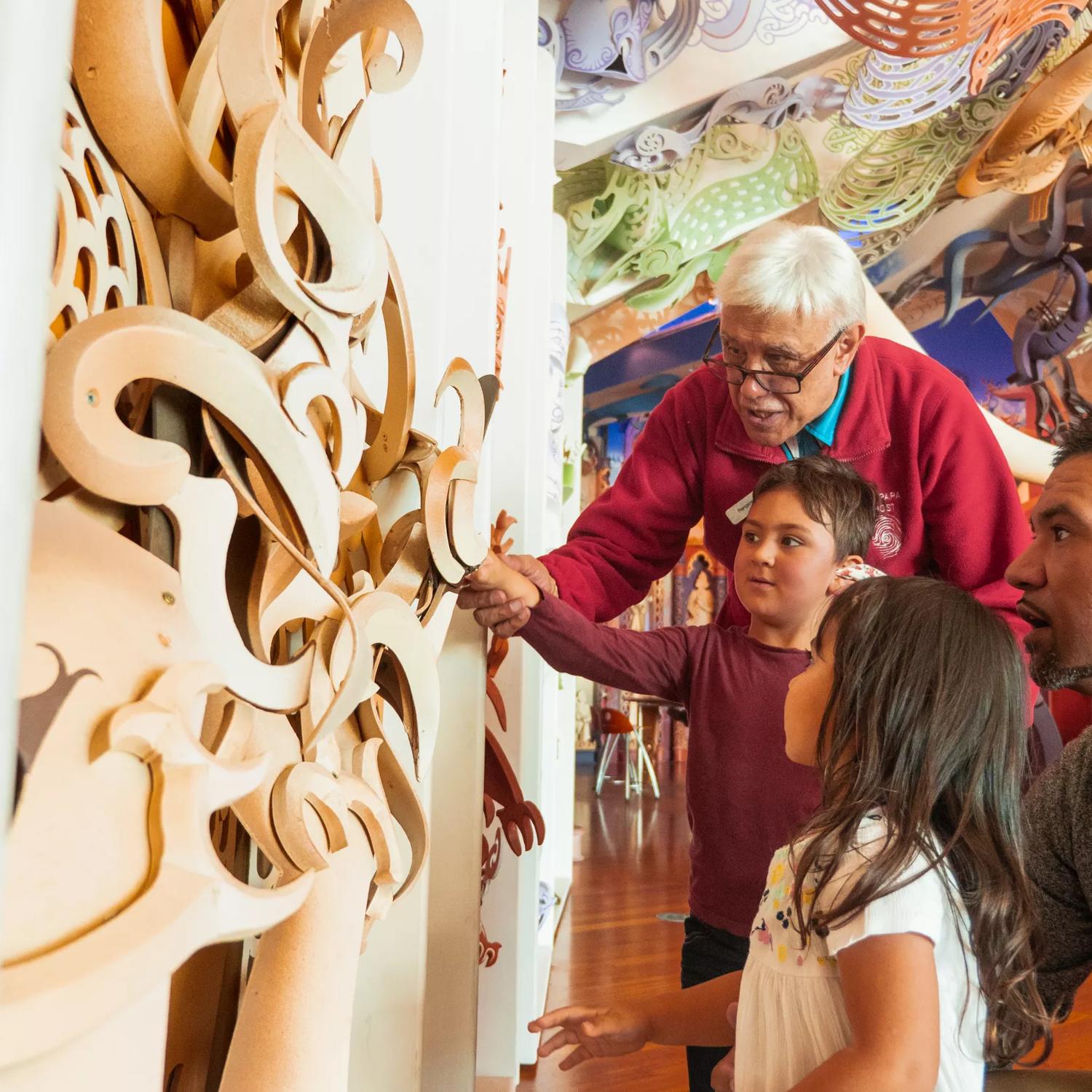 Two children and two adults are in a Maori exhibition in Te Papa Museum in Wellington admiring the woodwork that's displayed. 