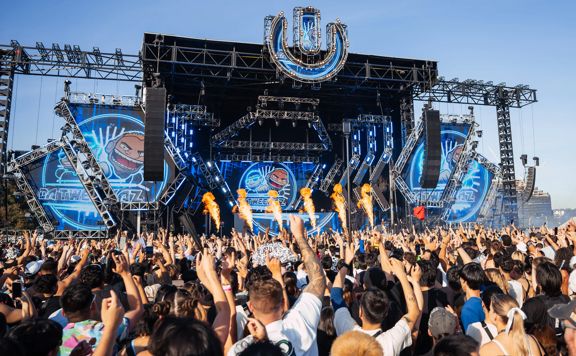 An outdoor stage at ULTRA Worldwide Music Festival in Melbourne, Australia, with huge screens, speakers, pyrotechnics, and a packed cheering audience.
