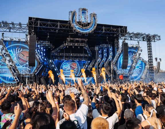 An outdoor stage at ULTRA Worldwide Music Festival in Melbourne, Australia, with huge screens, speakers, pyrotechnics, and a packed cheering audience.