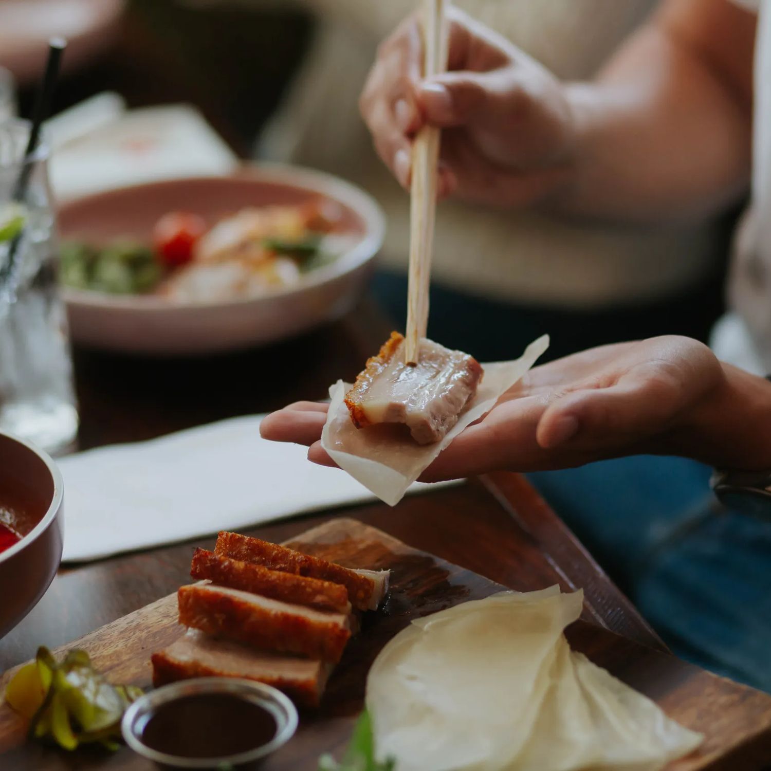 A diner uses chopsticks to assemble a bite on a rice cracker from a shared platter during a casual meal at a CHOW restaurant.