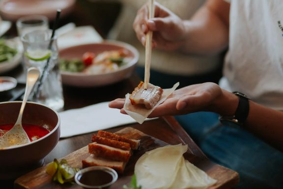 A diner uses chopsticks to assemble a bite on a rice cracker from a shared platter during a casual meal at a CHOW restaurant.
