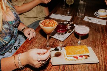 A person scoops cream from a caramel cocktail in The Library bar. Known for its desserts and drinks, a few colourful sweet treats are sprawled around the table.
