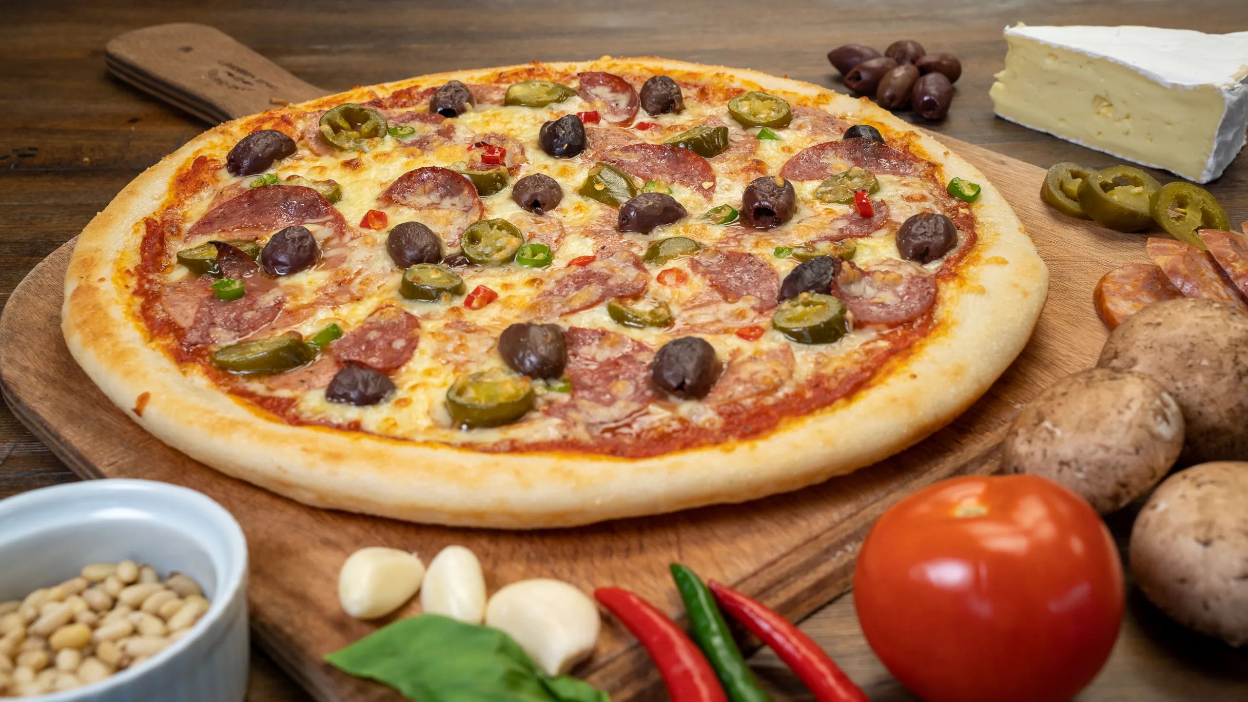 A pizza at Bogarts Pizzeria on a wooden chopping board with vegetables around it.