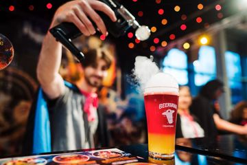 A person holds a tool applying smoke to the top of a pint of red and yellow beer at Beervana 2023, a beer and food festival in Wellington New Zealand.