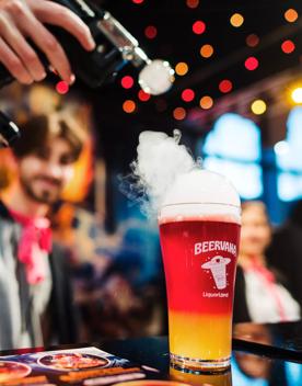 A person holds a tool applying smoke to the top of a pint of red and yellow beer at Beervana 2023, a beer and food festival in Wellington New Zealand.