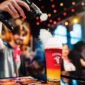 A person holds a tool applying smoke to the top of a pint of red and yellow beer at Beervana 2023, a beer and food festival in Wellington New Zealand.