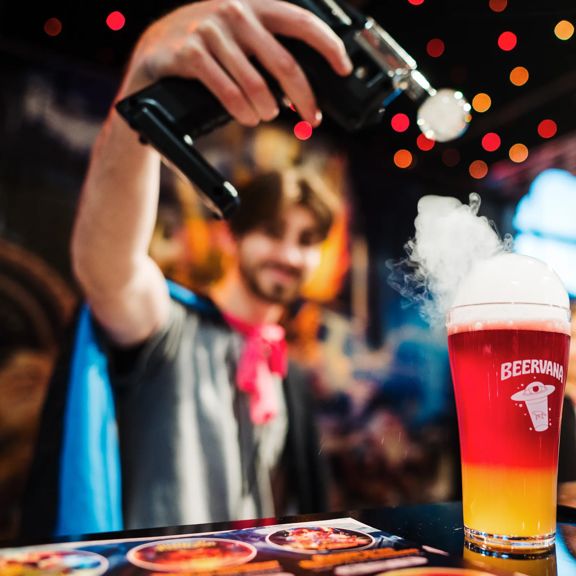 A person holds a tool applying smoke to the top of a pint of red and yellow beer at Beervana 2023, a beer and food festival in Wellington New Zealand.