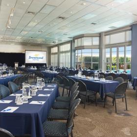 Rectangle shaped room with over 100 chairs around tables facing towards a projector at the front of the room.