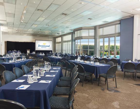 Rectangle shaped room with over 100 chairs around tables facing towards a projector at the front of the room.