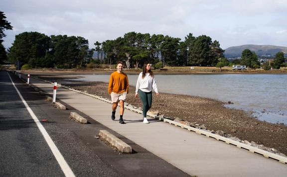 Two people walking on the roadside pathway around Pāuatahanui inlet.