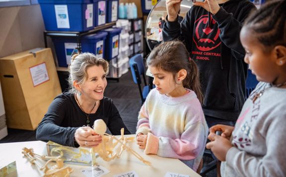 A teacher shows a miniature model skeleton to a few young students.