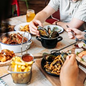 Three people eat crab and other seafood plates at The Crab Shack on Queens Wharf.