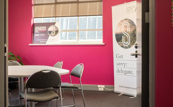 A meeting room with a hot pink accent wall at the Strictly Savvy office, a virtual assistant company based in Upper Hutt. 