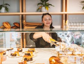 A server uses tongs to pick up a pastry from a glass cabinet.
