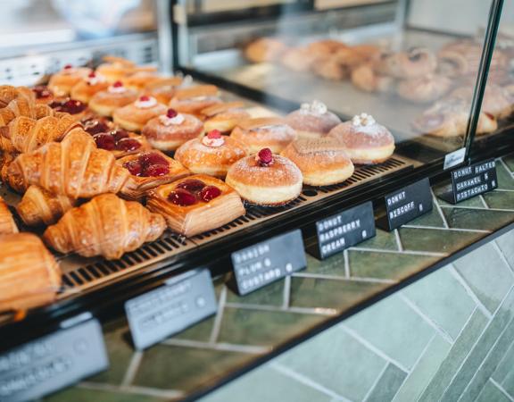 Rows of assorted pastries in a glass display case on a green-tiled counter top. 