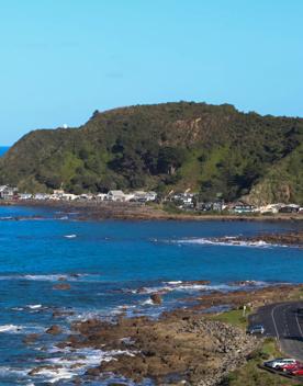 Breaker Bay on a sunny day, blue and green waves crashing on the stoney shore, with green cliffs surrounding.