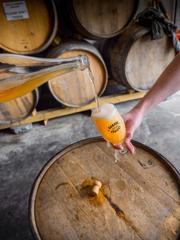 Inside the Wild Workshop, Garage Project’s second brewery situated in the busy Cuba Street precinct. Beer is being poured into a branded glass with barrels seen in the background.