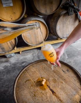 Inside the Wild Workshop, Garage Project’s second brewery situated in the busy Cuba Street precinct. Beer is being poured into a branded glass with barrels seen in the background.