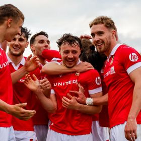 Players from Wrexham AFC huddle together in celebration, they wear read and white shirts.