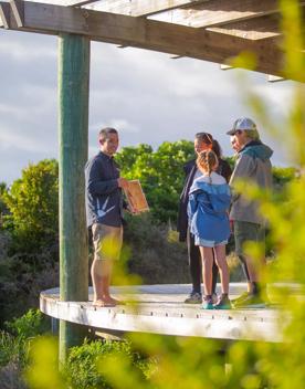 A tour guide talks to a family on a wooden deck.
