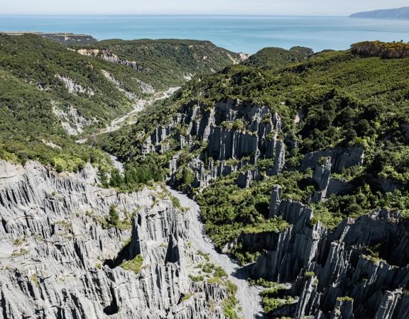 Image of the Pūtangirua Pinnacles. Taken from a drone, looking down on the large stalagmite structures, with Palliser Bay in the background.