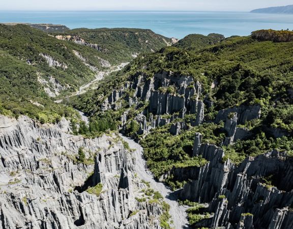 Image of the Pūtangirua Pinnacles. Taken from a drone, looking down on the large stalagmite structures, with Palliser Bay in the background.