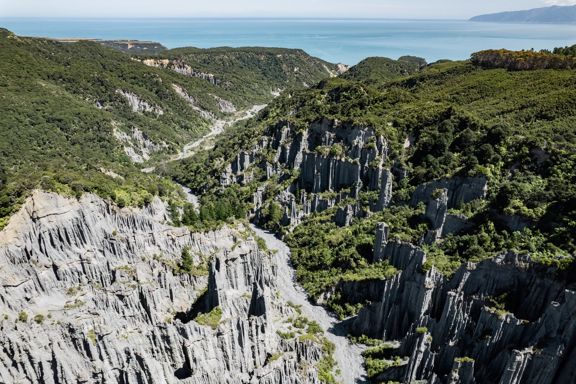 Image of the Pūtangirua Pinnacles. Taken from a drone, looking down on the large stalagmite structures, with Palliser Bay in the background.