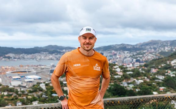 David Haunschmidt wearing an orange t shirt, with the Wellington city skyline in the background.