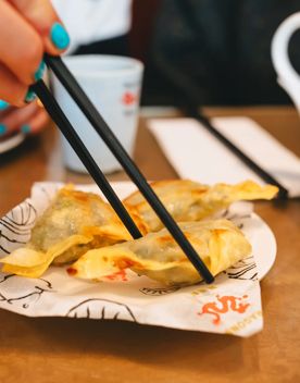 A small plate with three friend dumplings, one of which is being picked up by a pair of chopsticks.