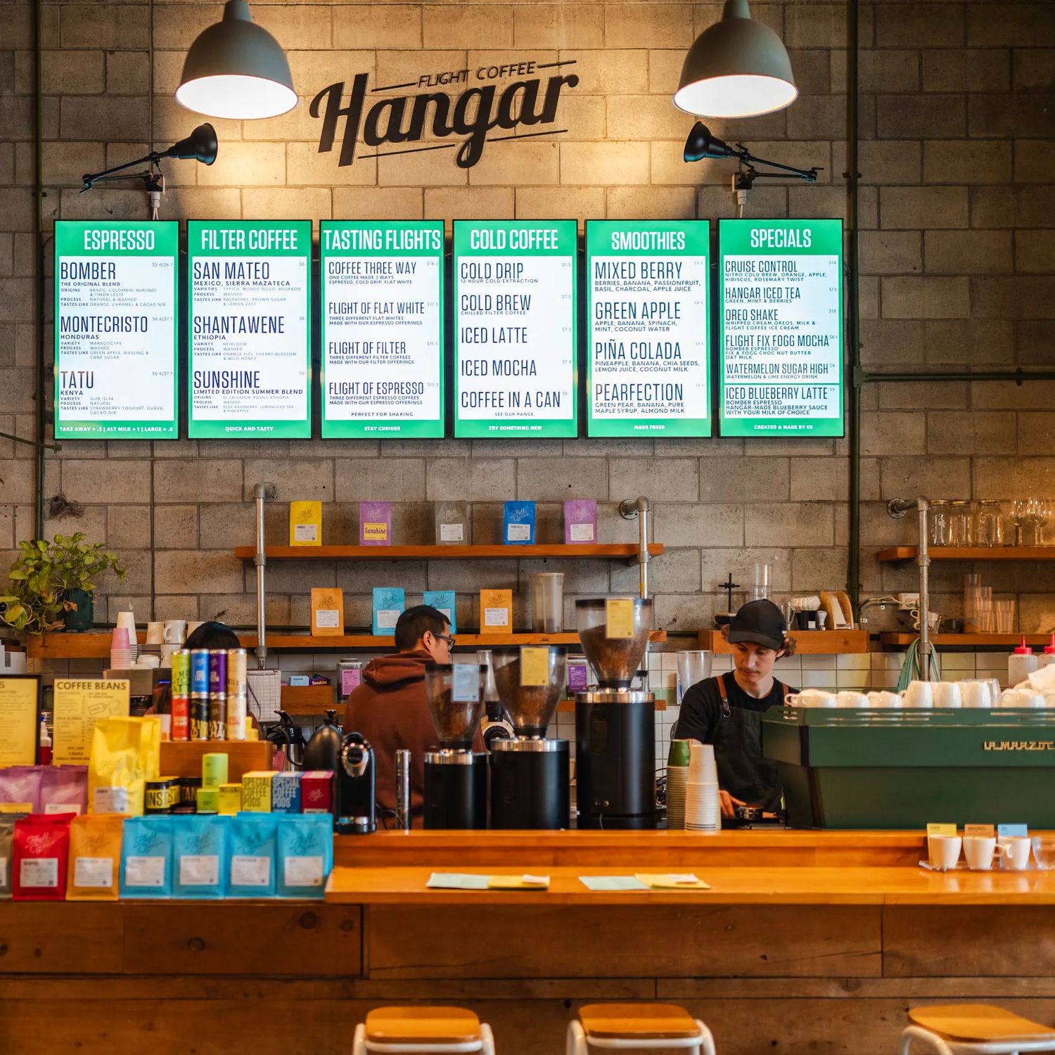 Inside The Hangar café. Two workers are behind the counter while a customer looks at the menu.