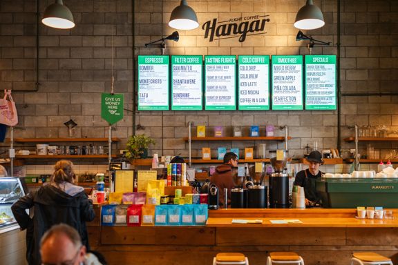 Inside The Hangar café. Two workers are behind the counter while a customer looks at the menu.
