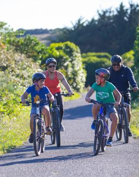Two adults and two children cycling along a wide, flat path in Queen Elizabeth Park, Kāpiti Coast.