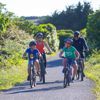 Two adults and two children cycling along a wide, flat path in Queen Elizabeth Park, Kāpiti Coast.