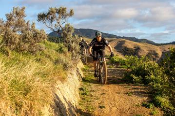 Two mountain bikers ride along a dirt track in the hills.