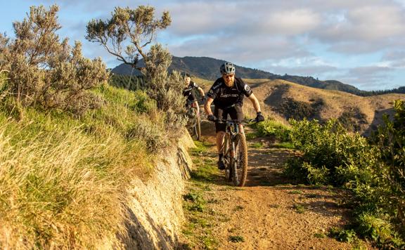 Two mountain bikers ride along a dirt track in the hills.