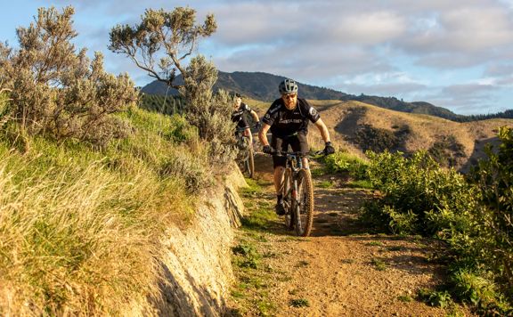 Two mountain bikers ride along a dirt track in the hills.