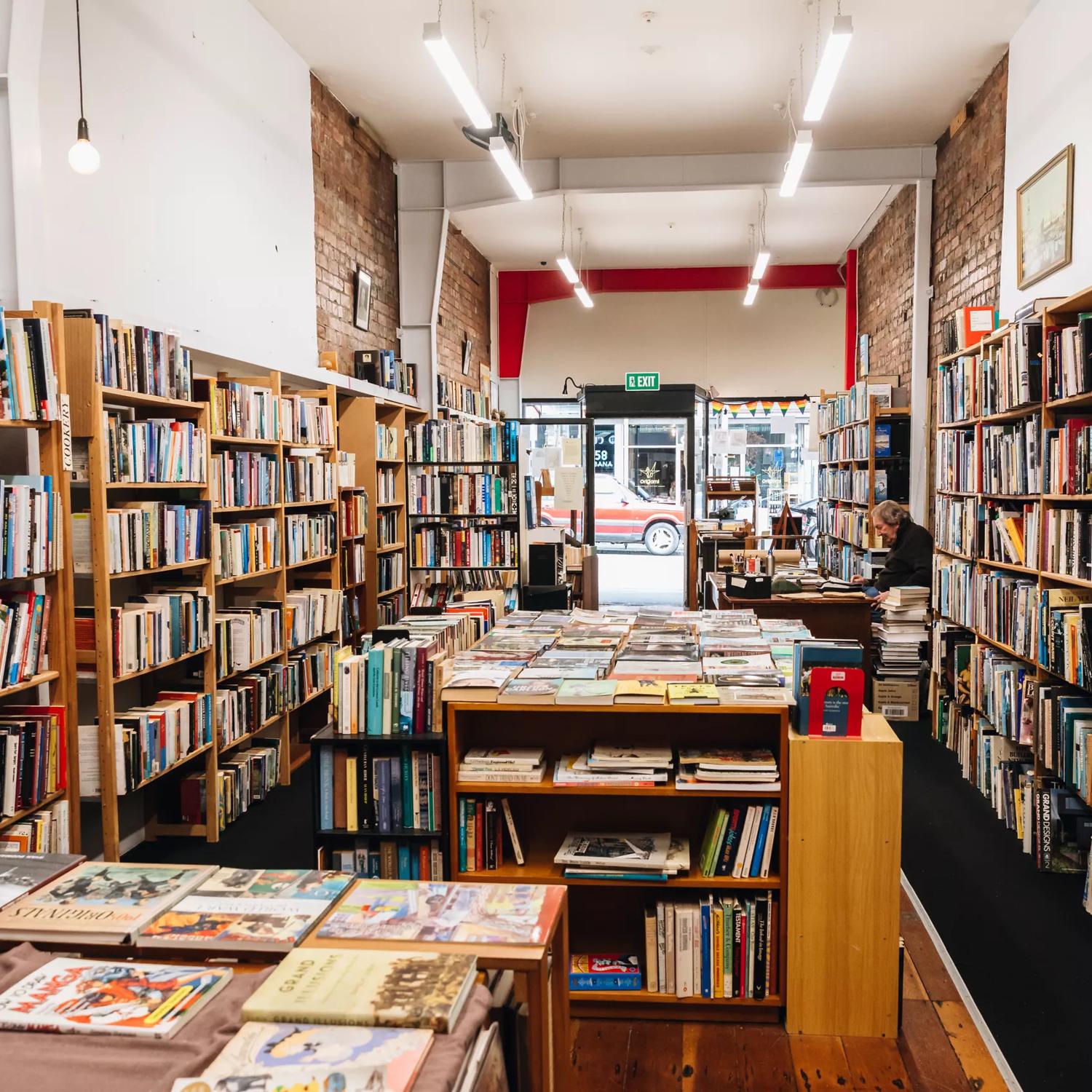 Inside The Ferret Bookshop, a book store on Cuba Street in Te Aro, Wellington. The narrow space is lined with shelves full of books and a worker sits behind the counter. 