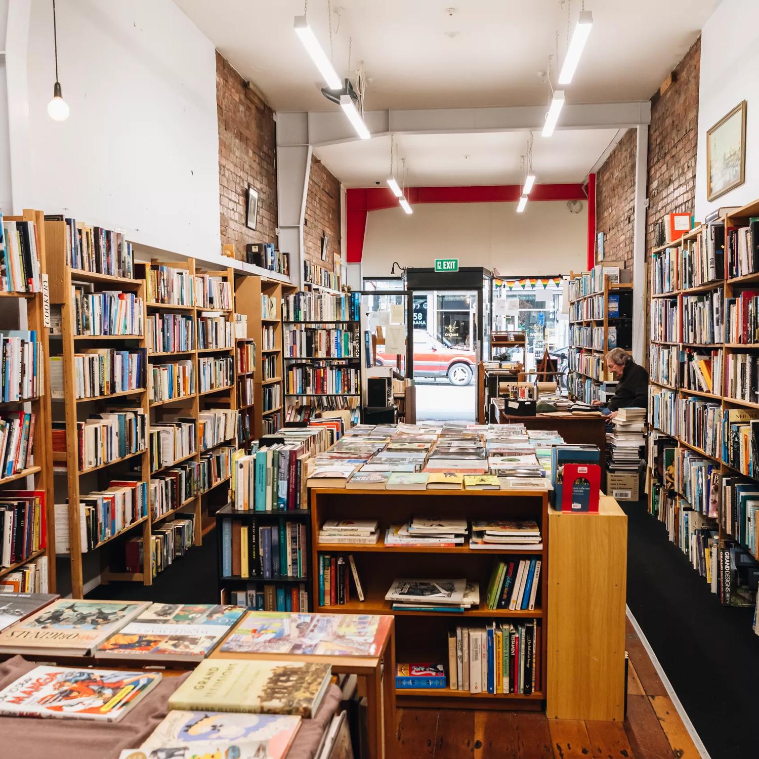 Inside The Ferret Bookshop, a book store on Cuba Street in Te Aro, Wellington. The narrow space is lined with shelves full of books and a worker sits behind the counter.