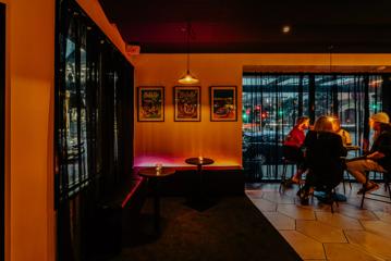 A cozy seating corner inside Plonk, with LED strip lighting in red and yellow, and carpeted floors next to the tiled ground underneath customers sitting at tables.