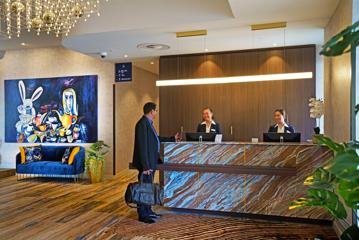 The concierge desk in the foyer of The Sebel, a 4-star hotel in Lower Hutt. Two hotel staff are behind the desk while a guest is checking in.