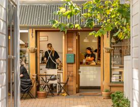 The exterior of Goods Manufactory & Bakery, with staff members baking inside and customers eating outside.