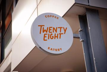 The sign outside of Twenty Eight, a café and eatery in Lower Hutt. It is a circular white sign with the restaurant's logo printed in orange.